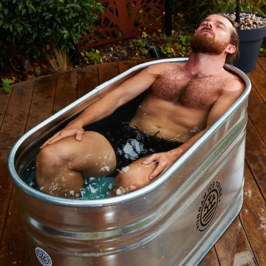 Man laying in a steel ice bath on decking in a garden