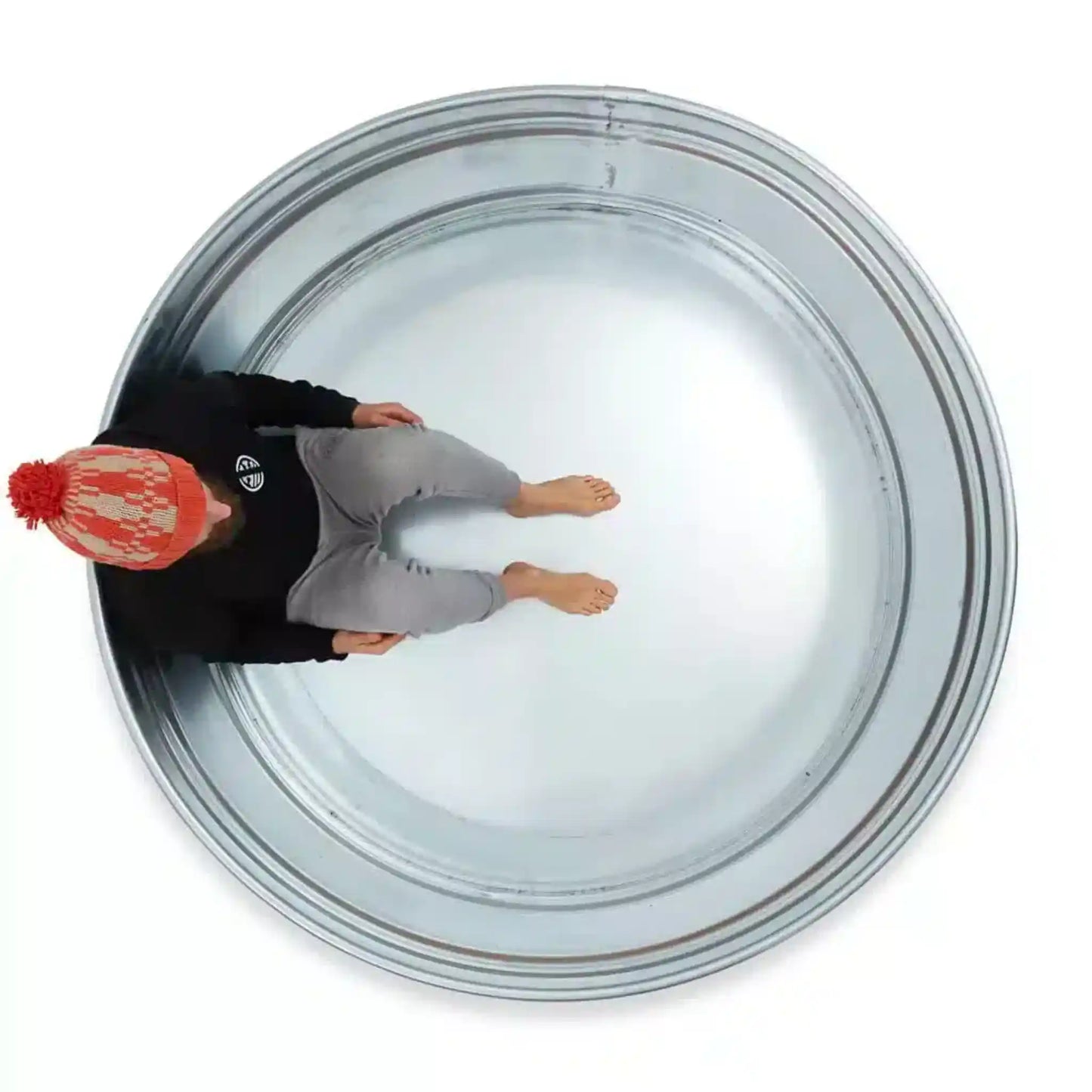 Person wearing a red beanie and black jacket inside a metal ice bath on a white background