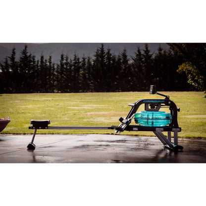 Rowing machine on a wet pavement with grass and trees in the background