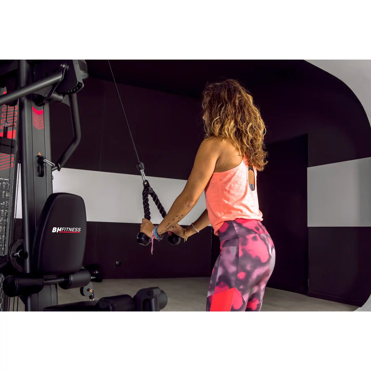 Woman using tricep extension function on a multi gym. 