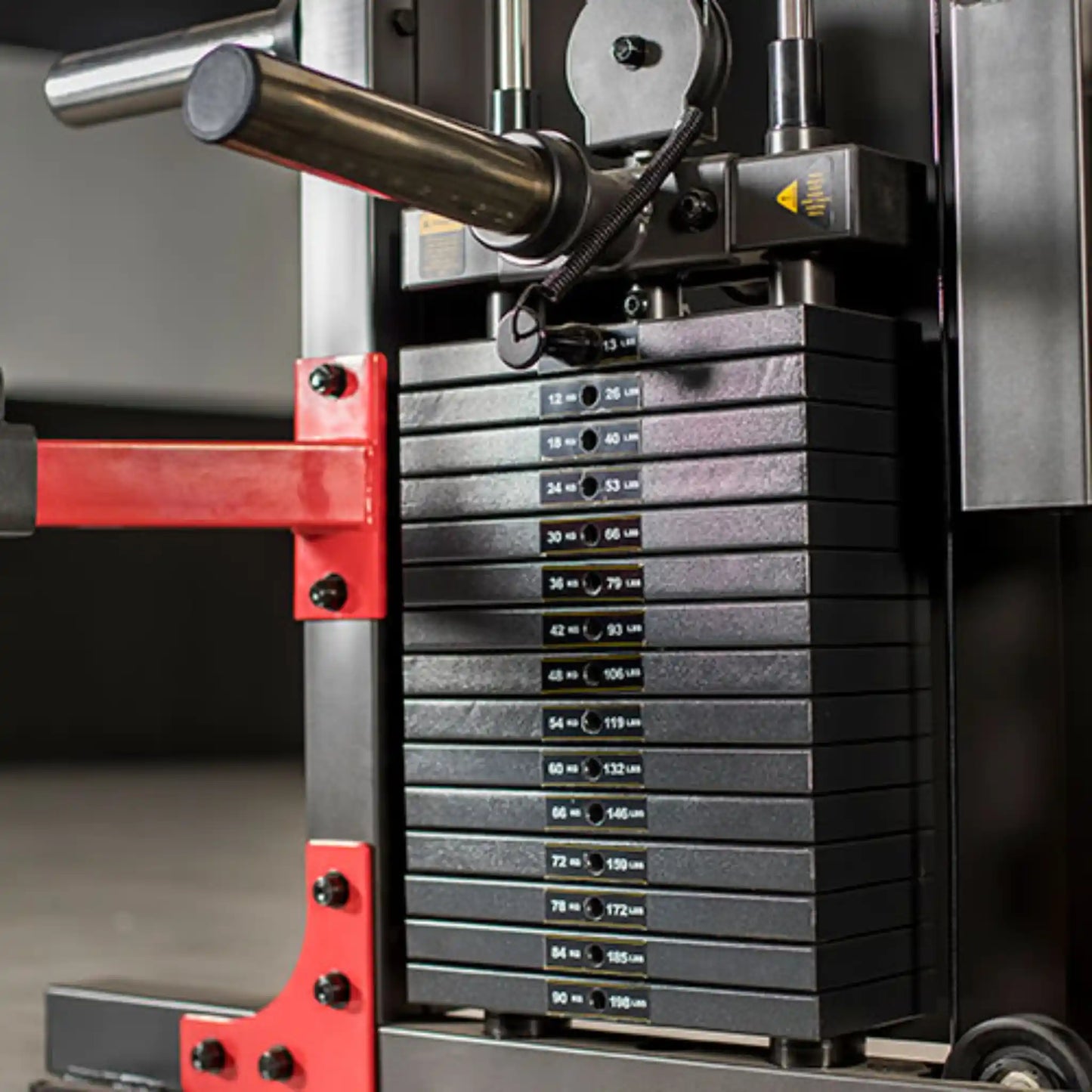 Stack of weight plates on a weightlifting machine with red safety bar