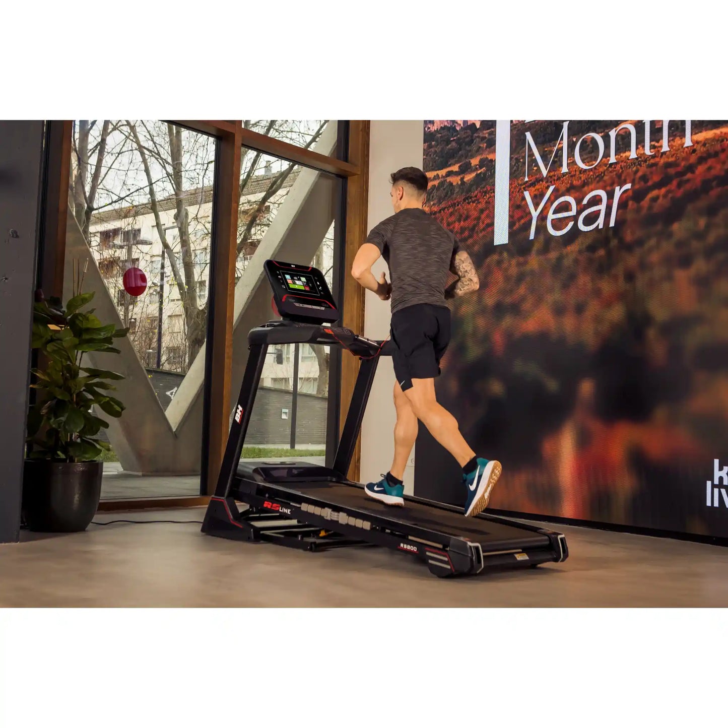 Man using a treadmill in a modern indoor setting with large windows.