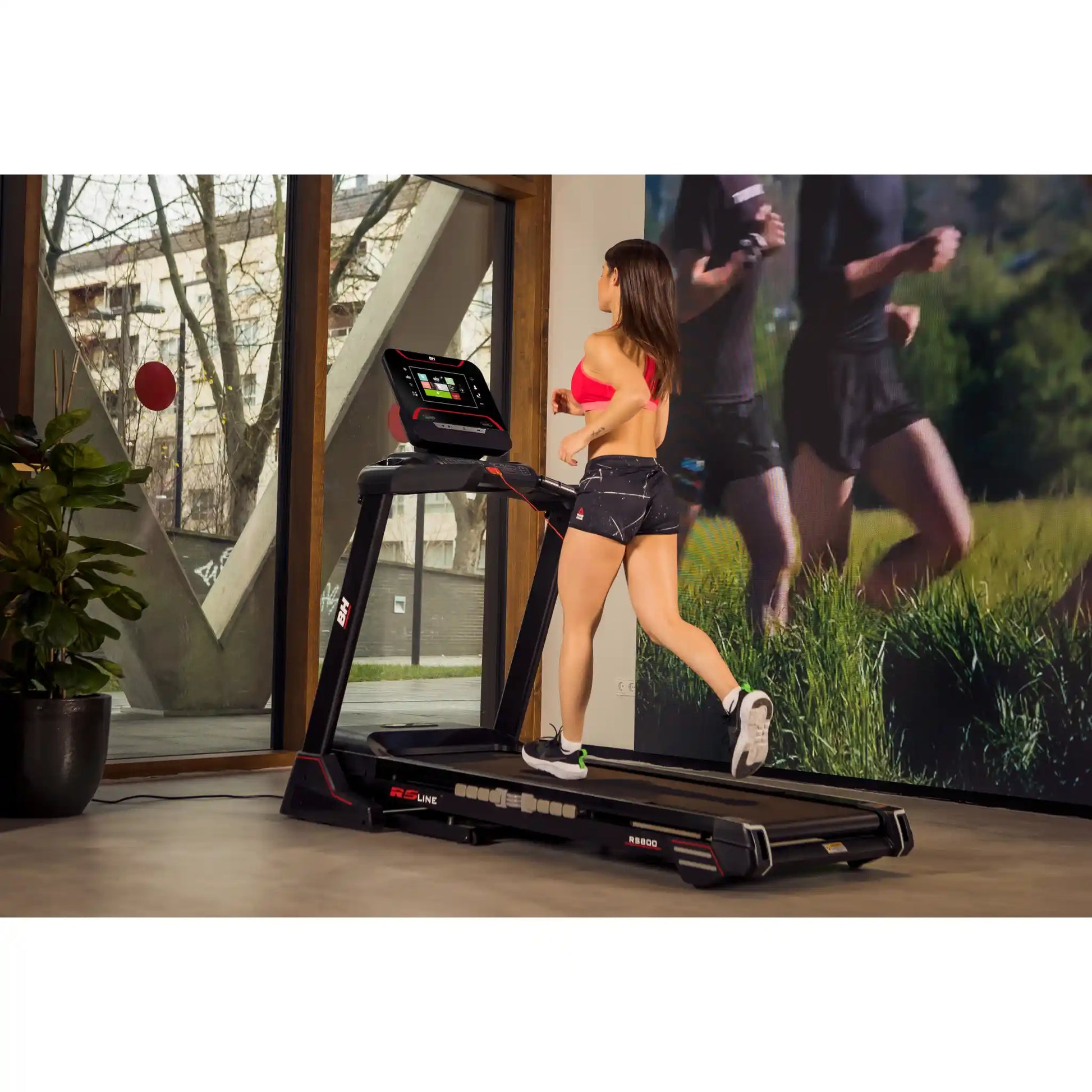 Woman running on a treadmill with a scenic display in a modern room.