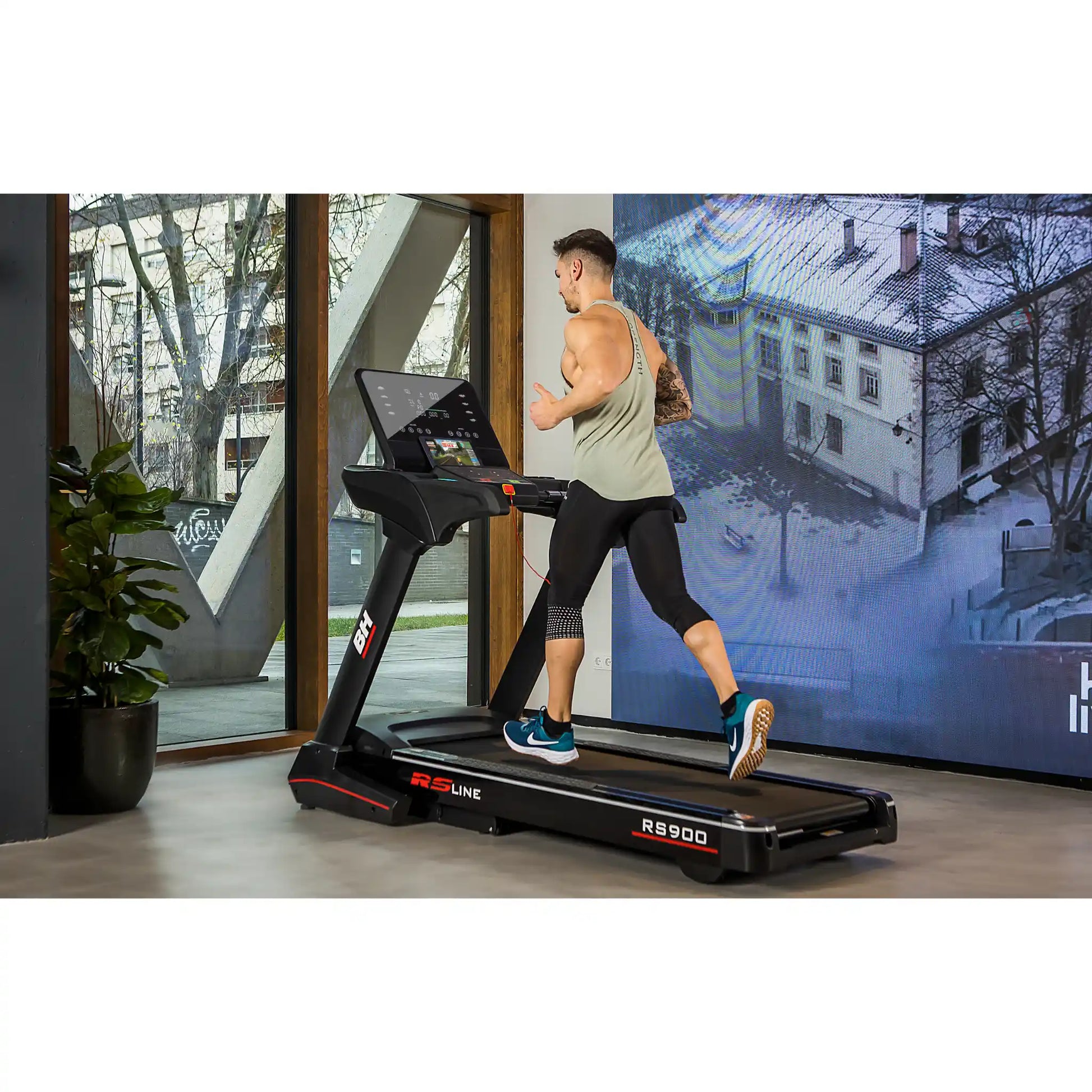 Person running on a treadmill in a modern indoor setting with a large screen displaying an outdoor scene.