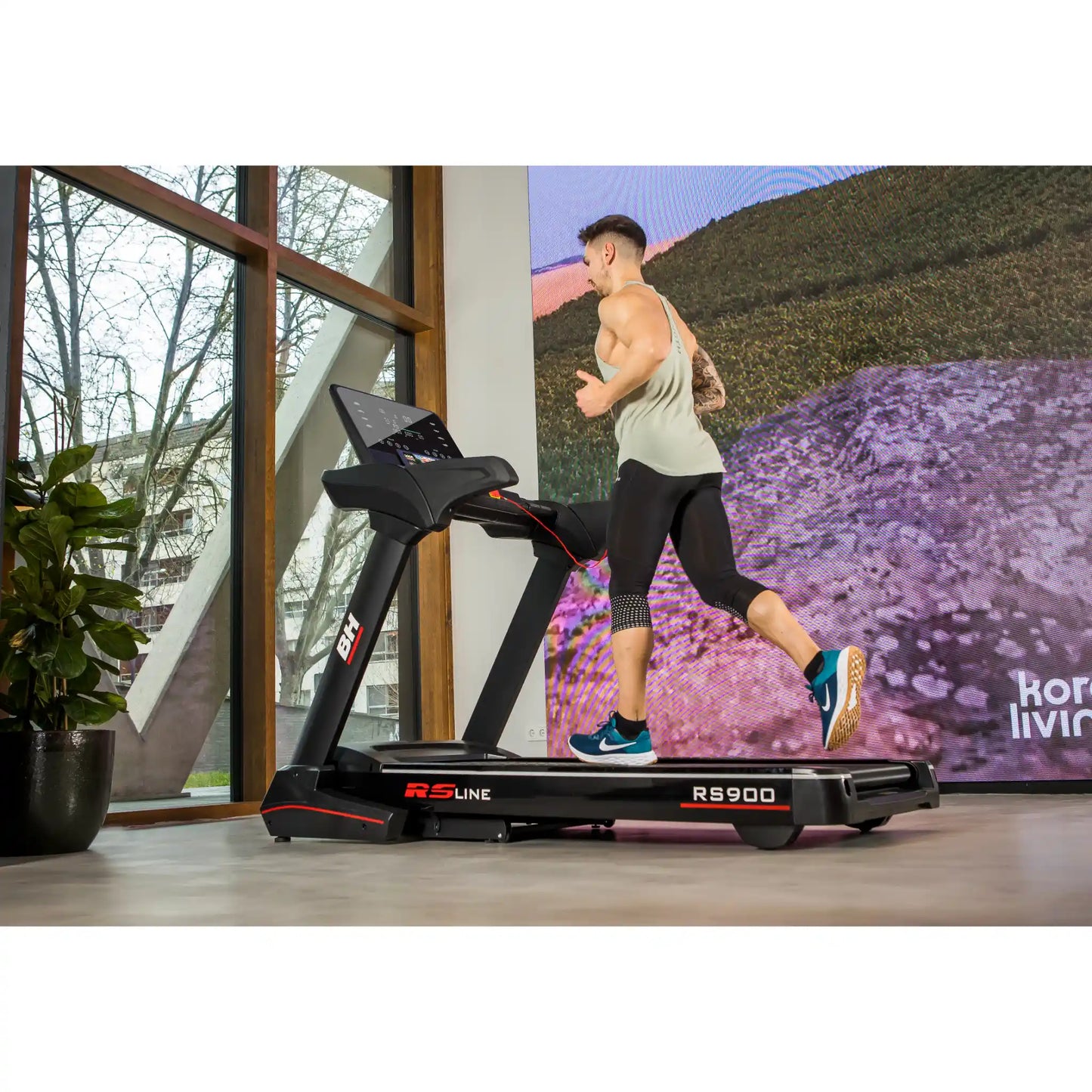 Person using a treadmill with a scenic display in a room with large windows.