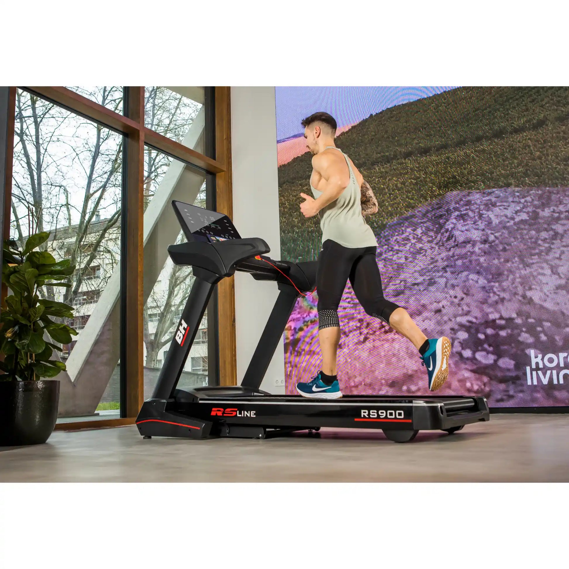 Person using a treadmill with a scenic display in a room with large windows.