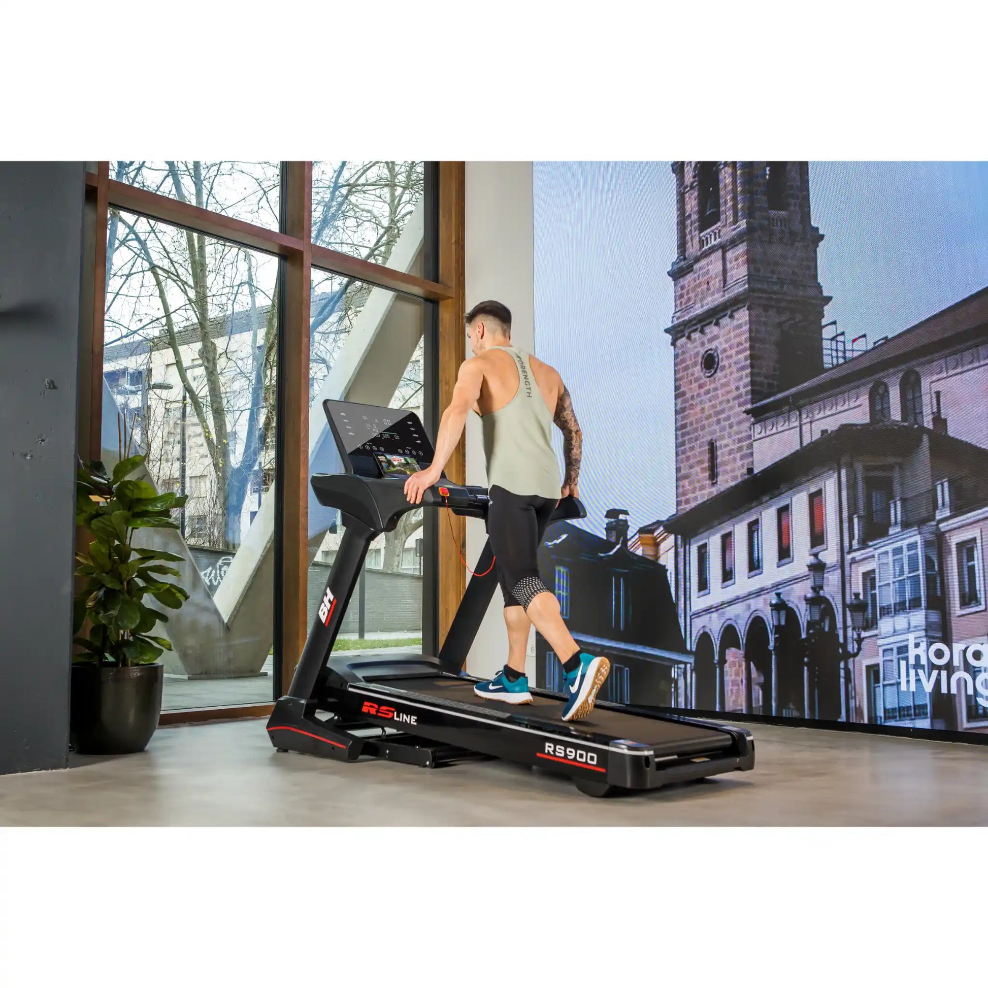 Person using a treadmill in a modern indoor setting with large windows.