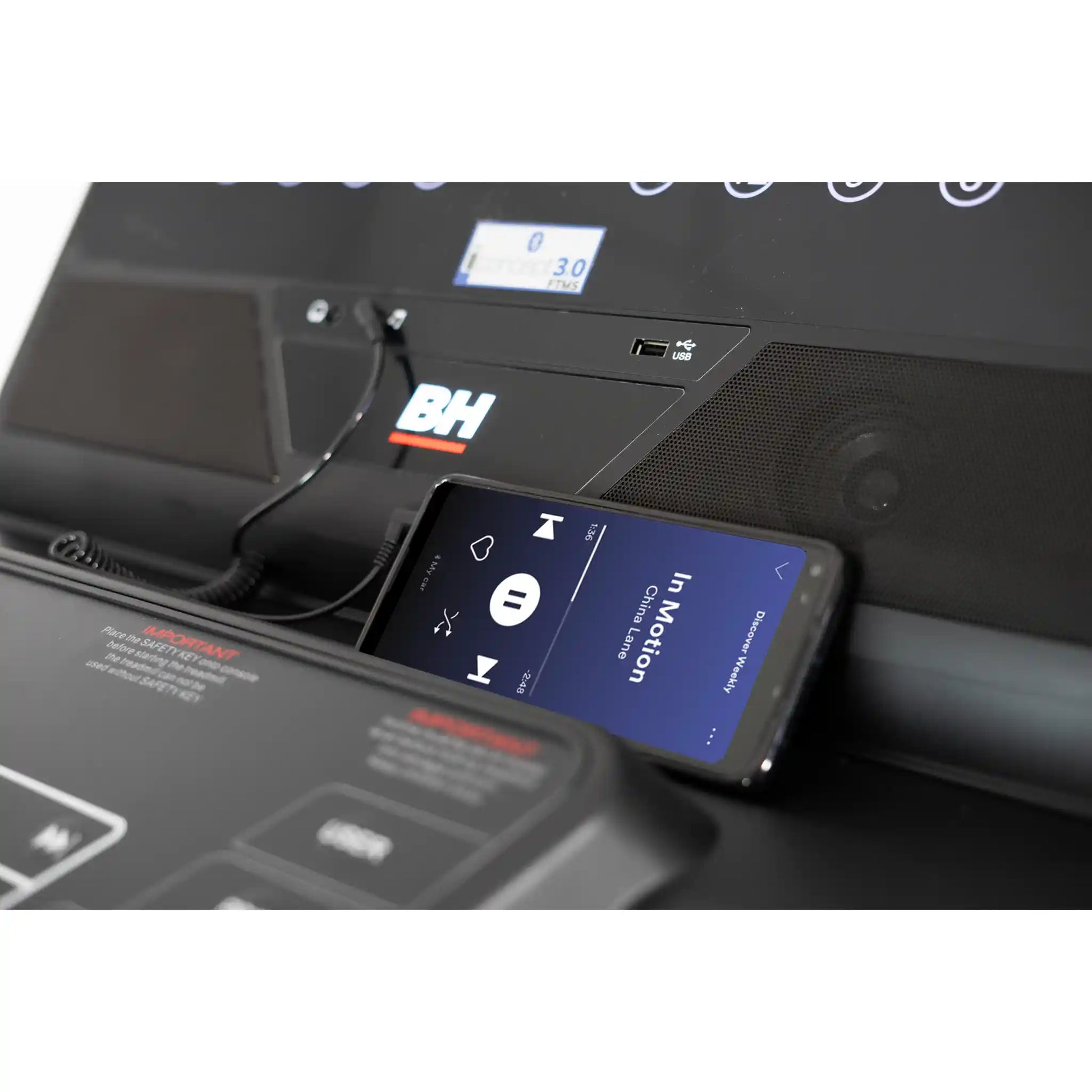 Phone displaying a music app on a treadmill with BH Fitness logo