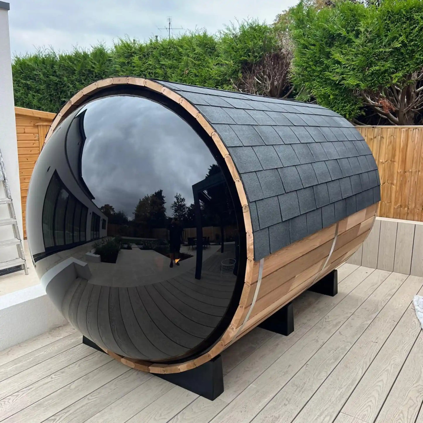 Modern outdoor barrel sauna with reflective window and wooden exterior on a wooden deck.