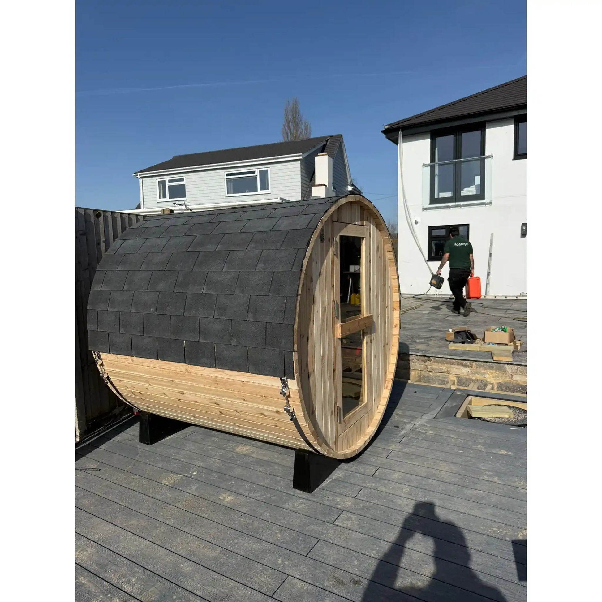 Wooden barrel-shaped sauna on a patio with a house in the background