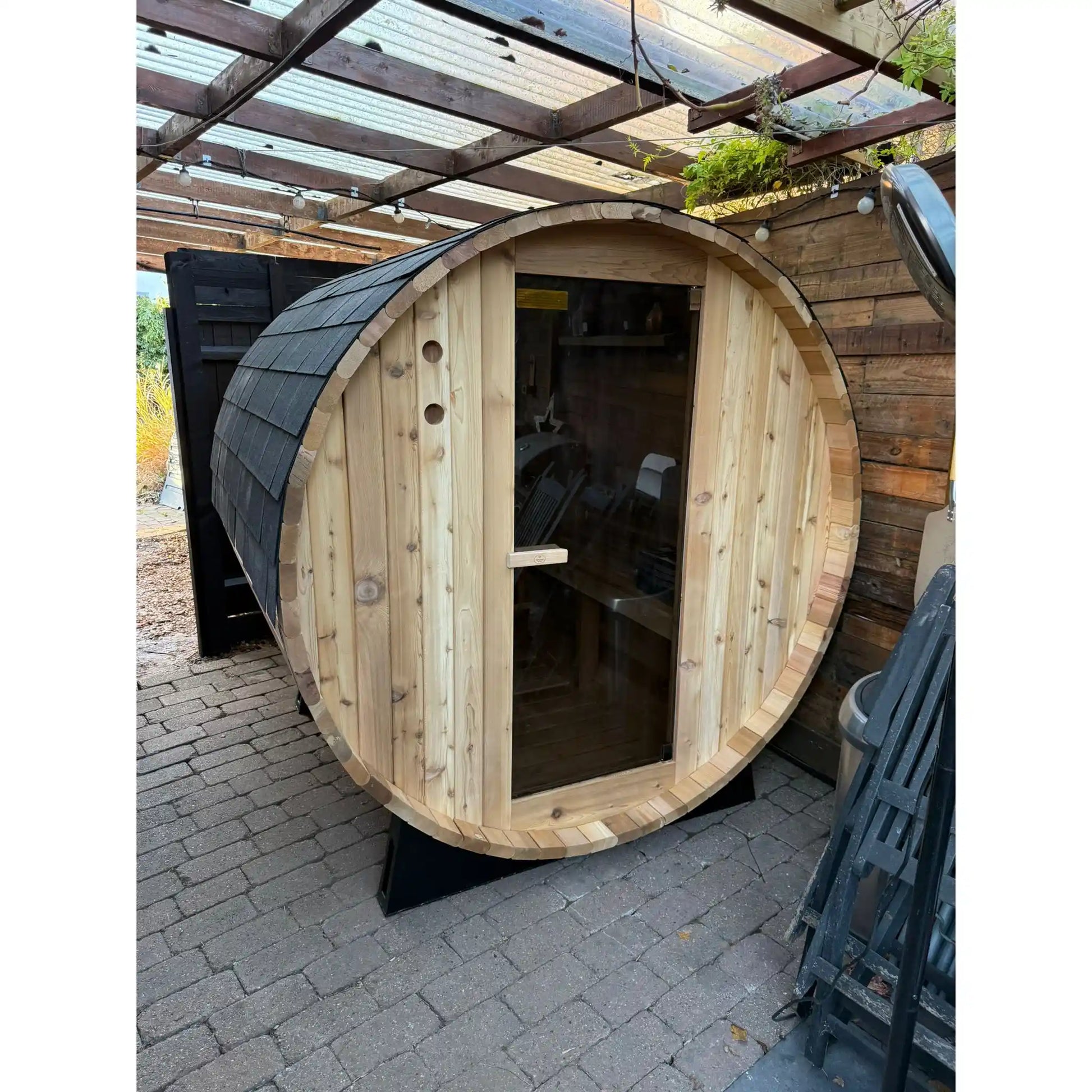 Wooden barrel sauna on a patio with outdoor furniture in the background