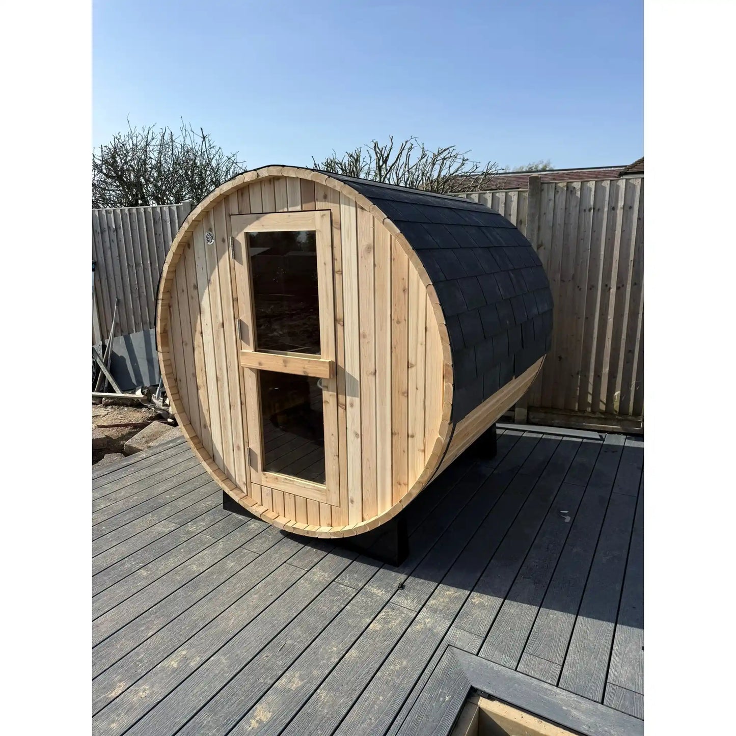 Wooden barrel-shaped sauna on a wooden deck with a clear sky background