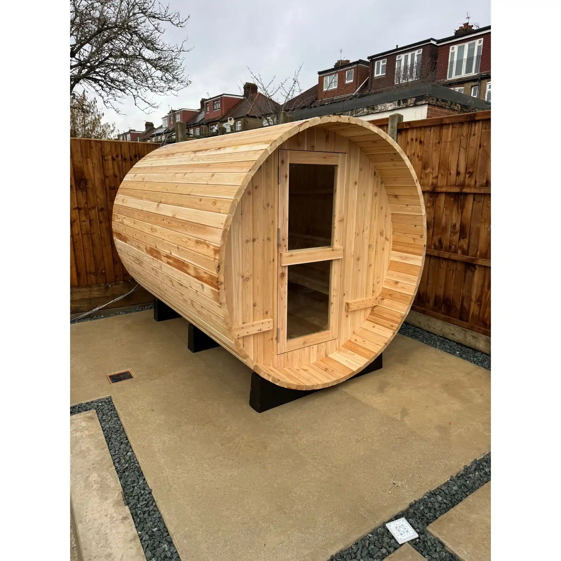 Wooden barrel-shaped sauna on a patio with houses in the background
