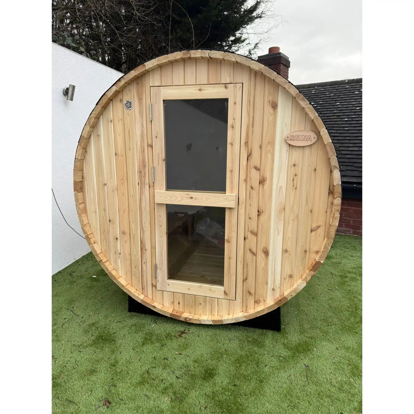 Wooden circular sauna on grass with a house in the background