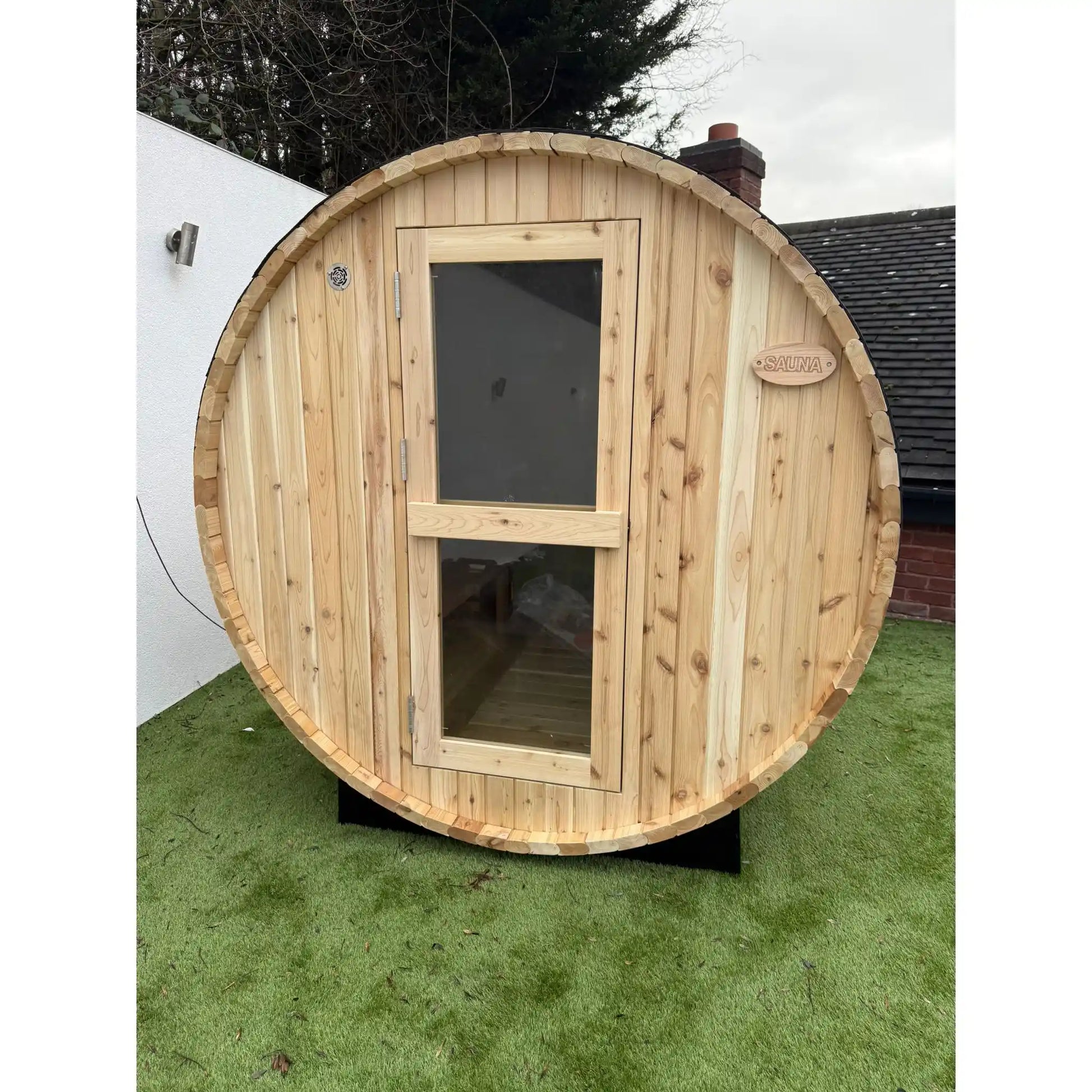 Wooden circular sauna on grass with a house in the background