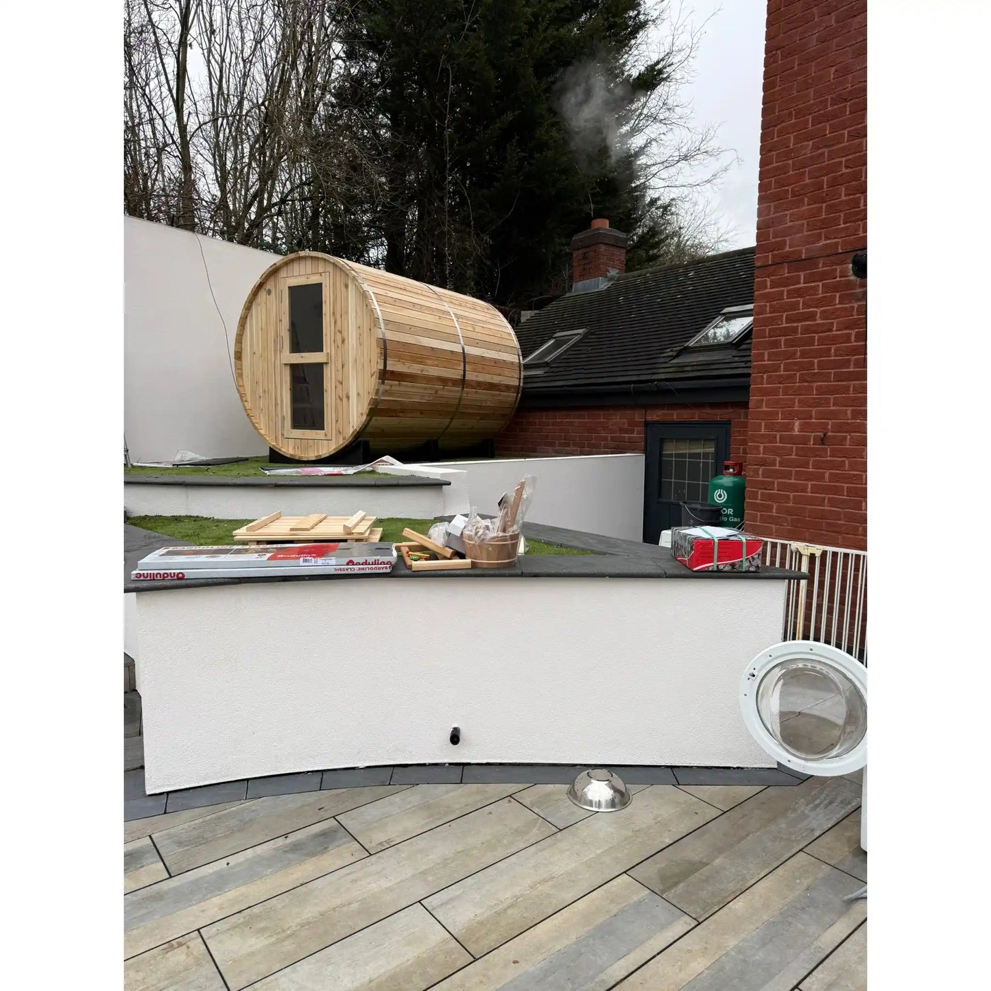 Wooden barrel on a white walled area of a garden with a house in the background