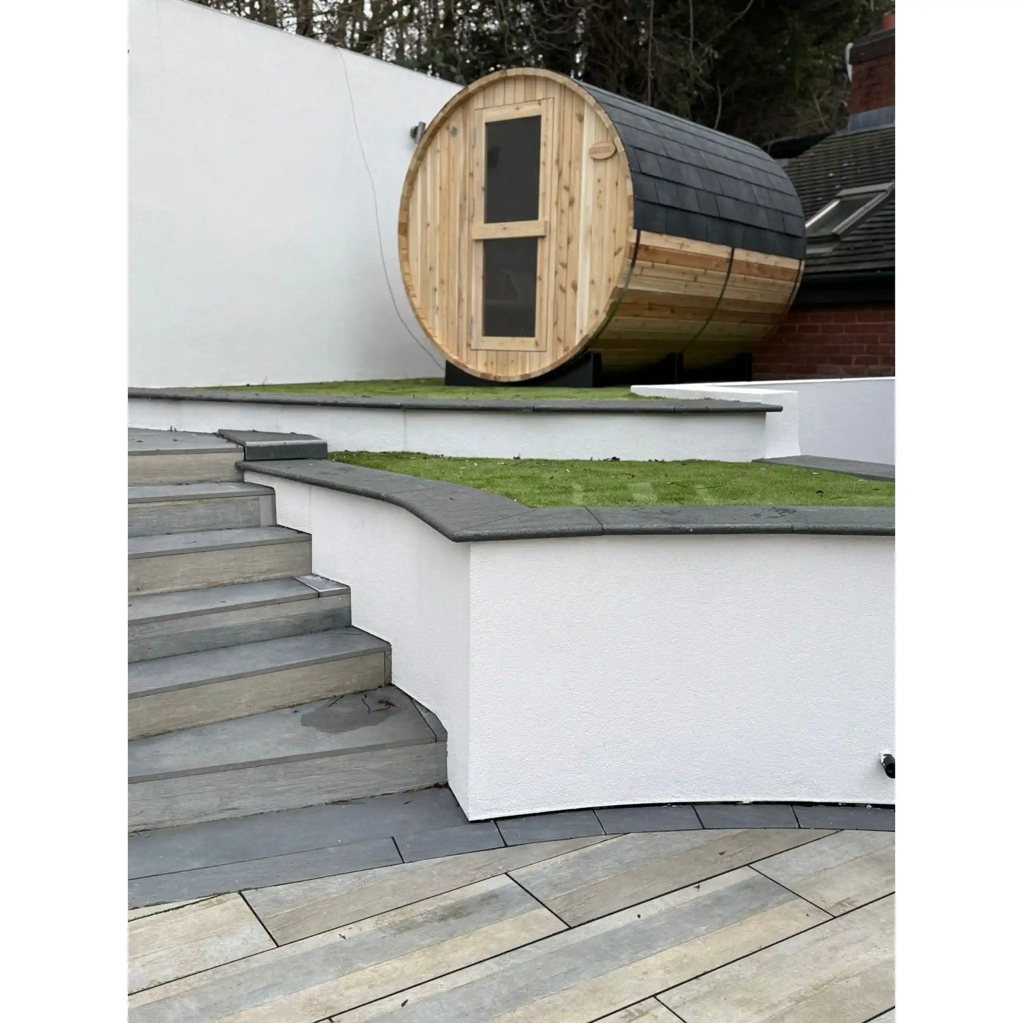Wooden barrel-shaped sauna in a white walled garden with greenery
