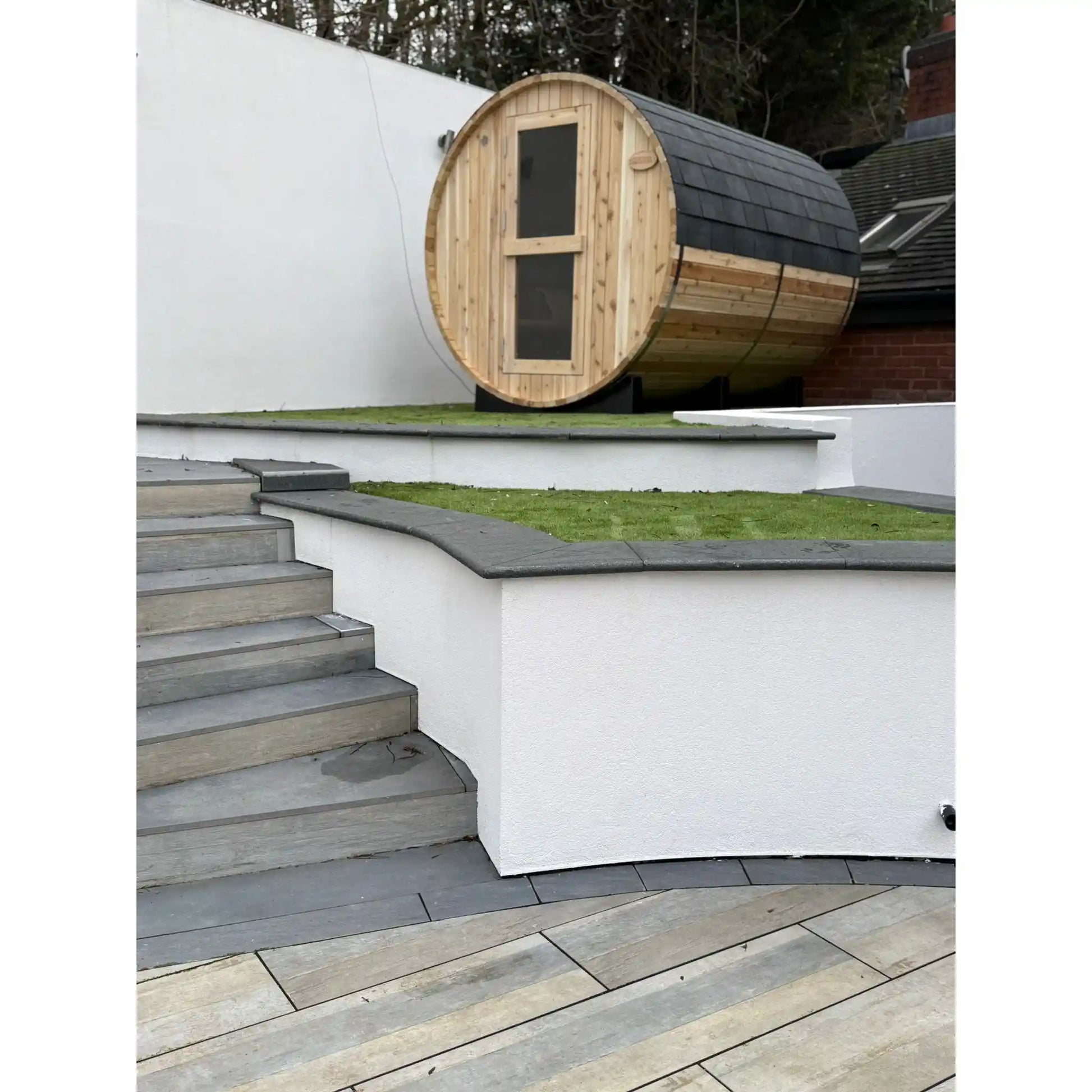 Wooden barrel-shaped sauna in a white walled garden with greenery