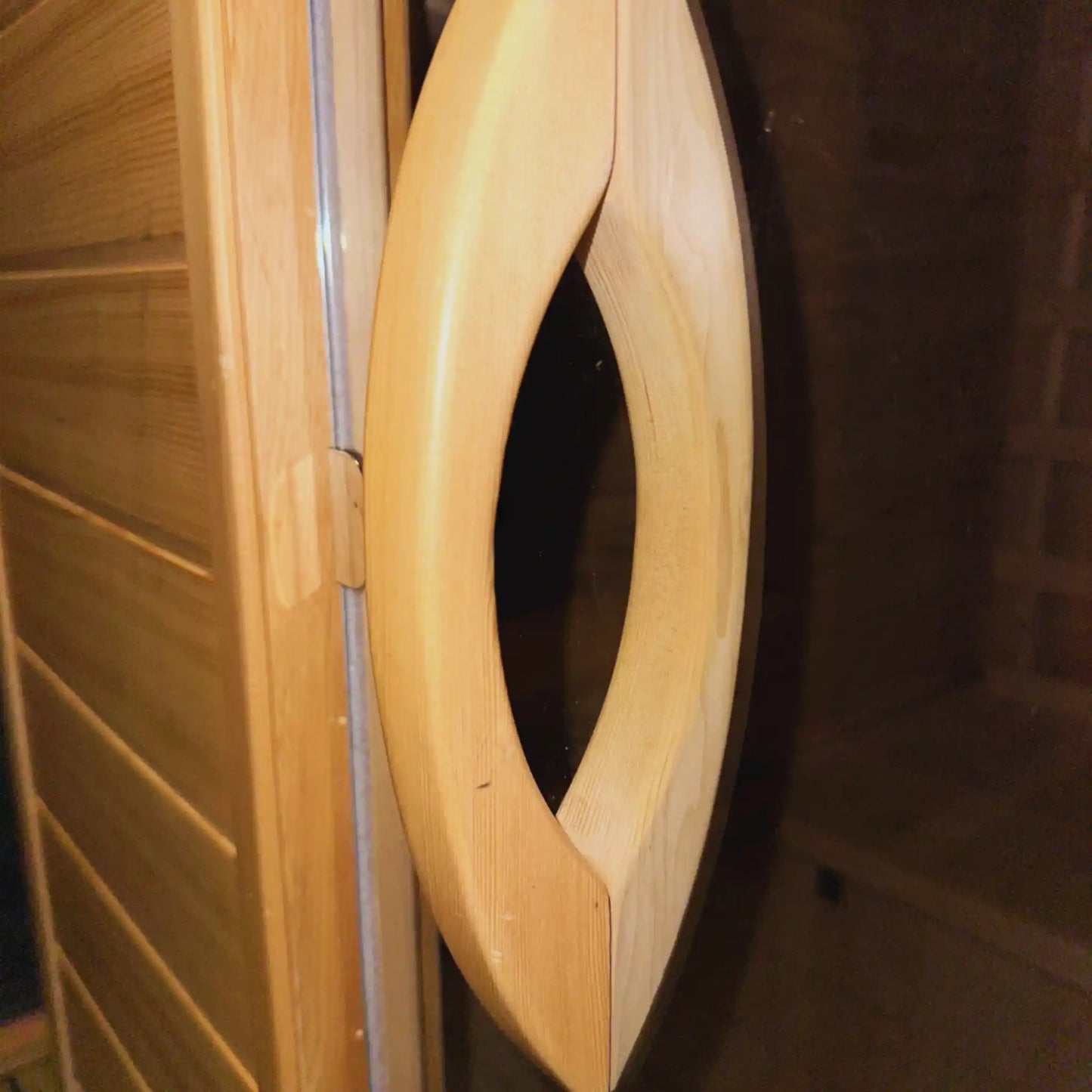 Wooden handle on glass sauna door with a dark background