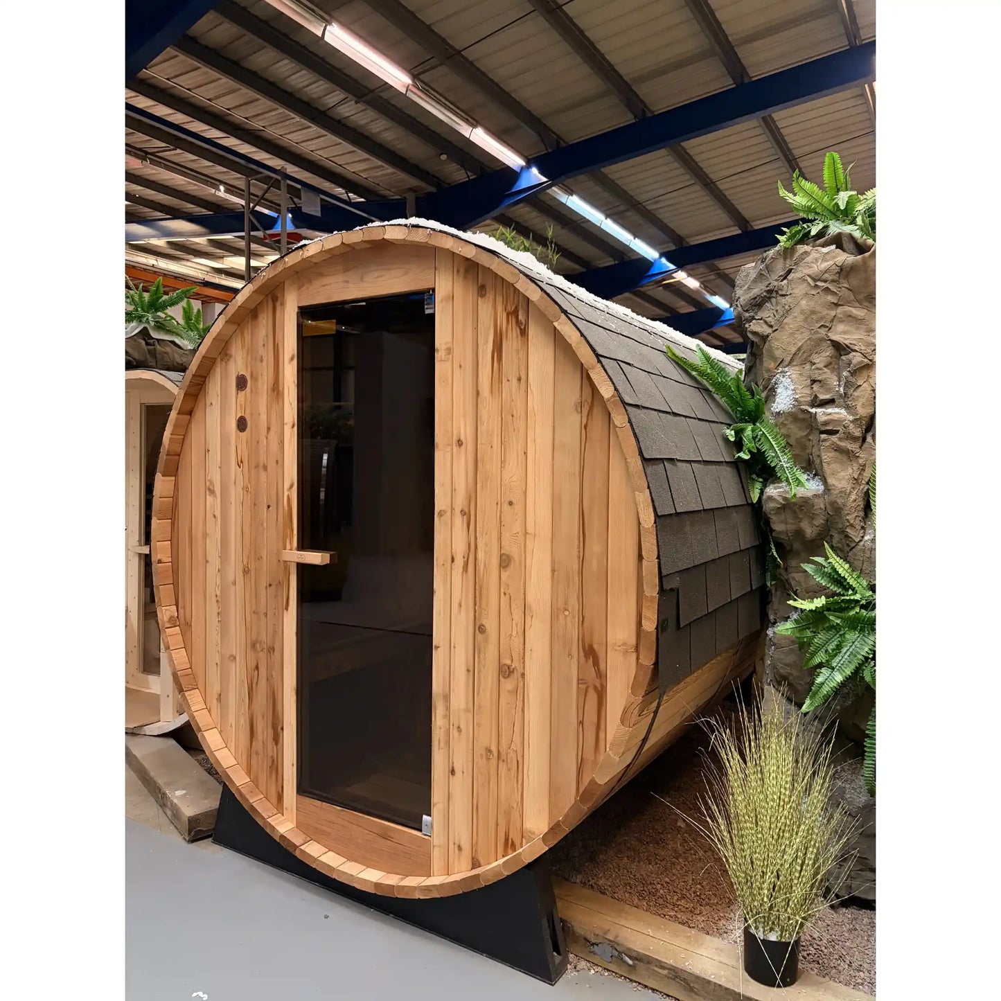 Wooden barrel-shaped sauna with a shingled roof in an indoor setting.