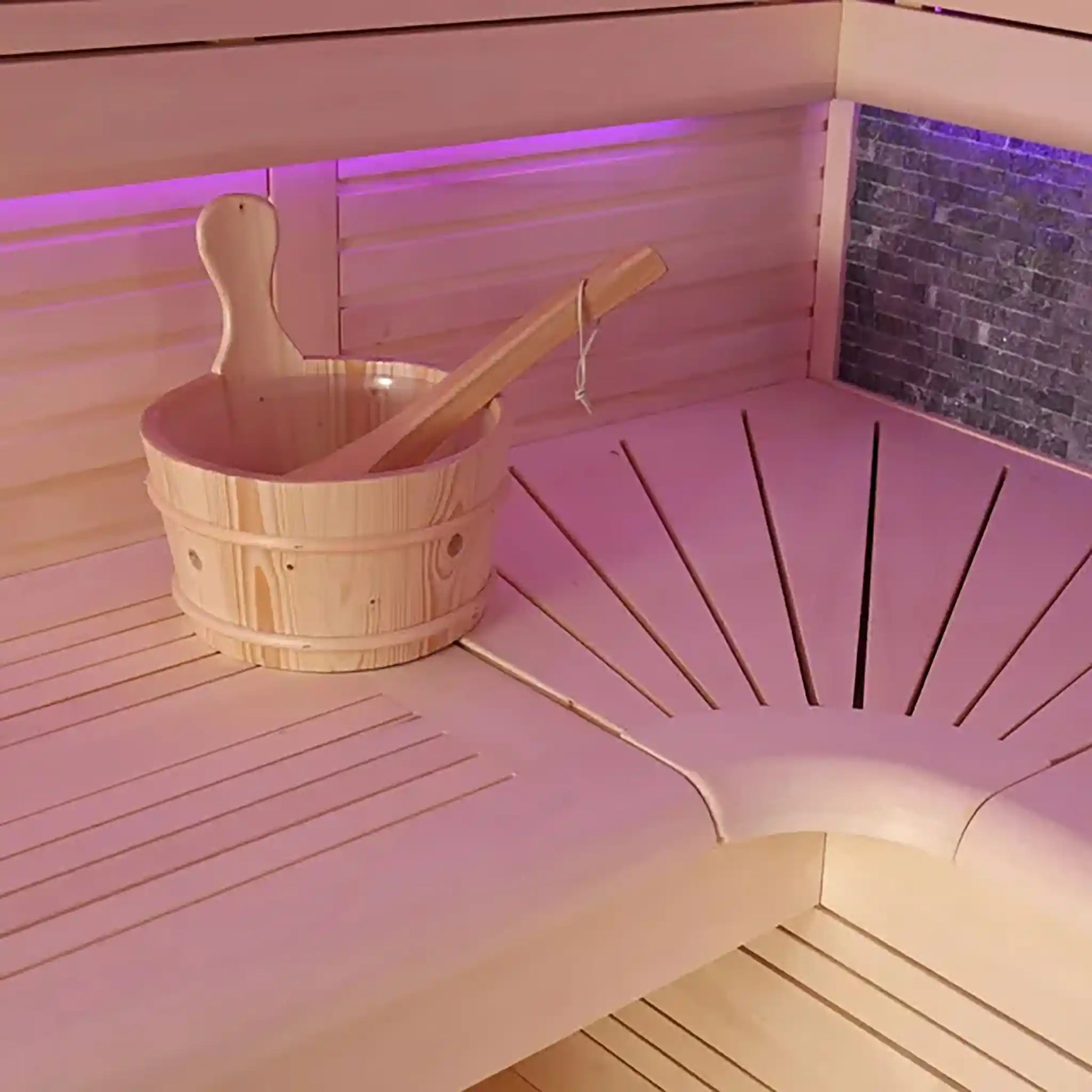 Wooden bucket and ladle on a bench in a sauna with pink lighting.