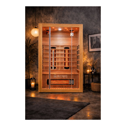 Infrared sauna with wooden interior and KOVE branding in a dimly lit room.