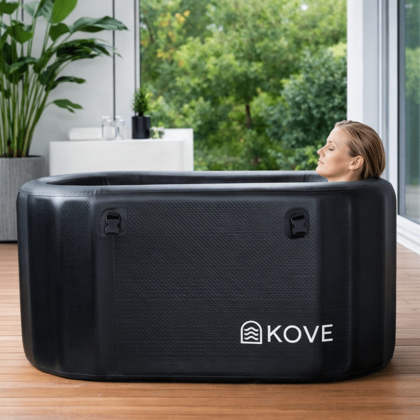 Person relaxing in a black Kove ice bath with a view of greenery outside.