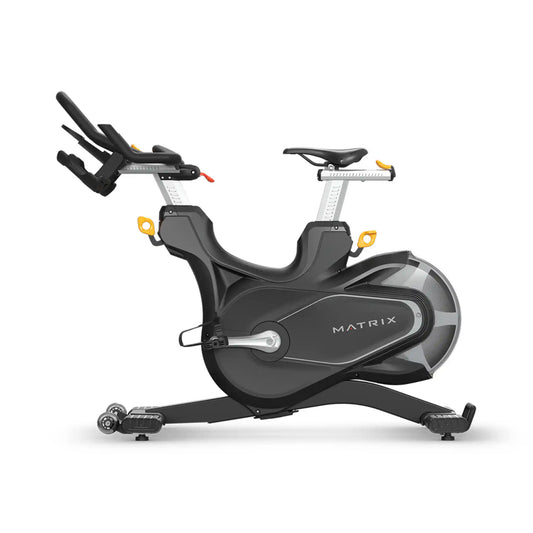 A Matrix brand indoor cycling machine in dark grey and black with silver metallic accents and small yellow adjustment knobs, shown from a side profile on a white background.
