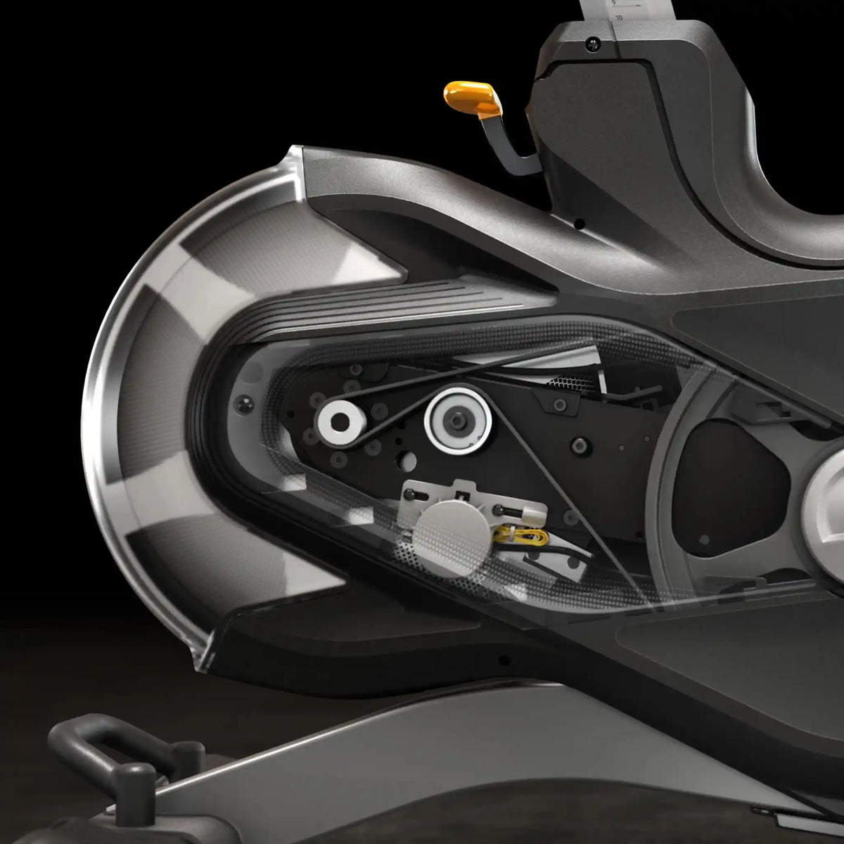 Close-up of the mechanics of a black exercise bike wheel, and part of the seat area against a dark studio background