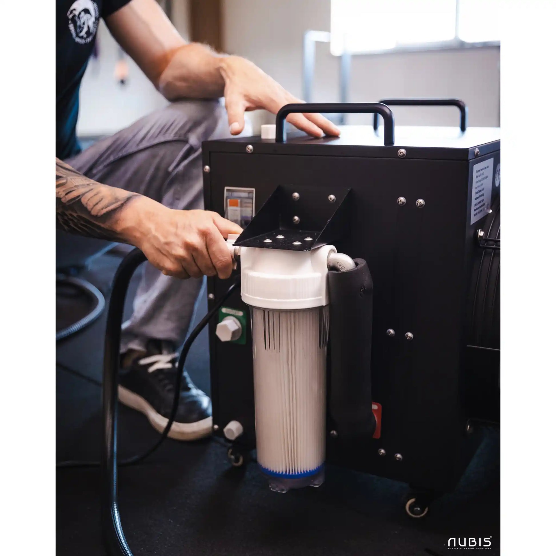 Person interacting with a black ice bath chiller with a filter, branded 'Nubis'.