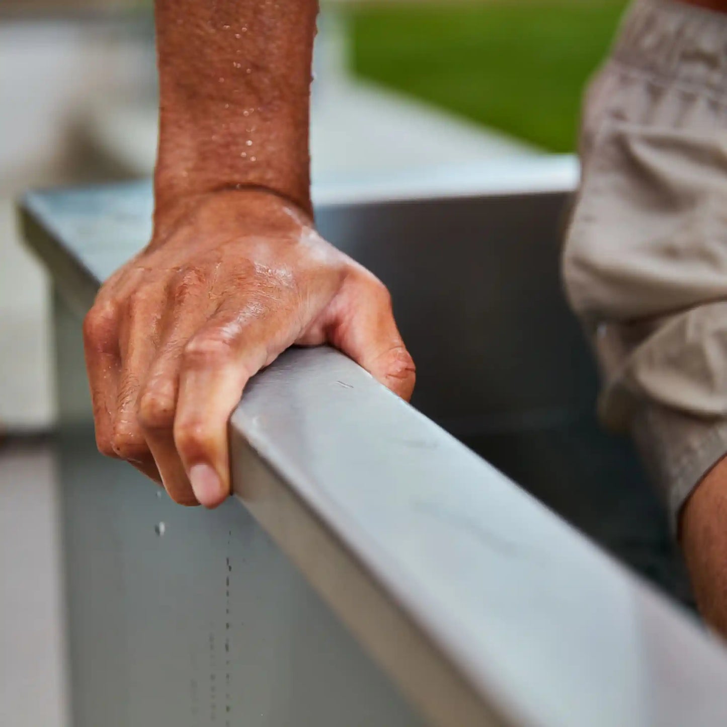 Hand holding onto side of a metal ice bath with a blurred background