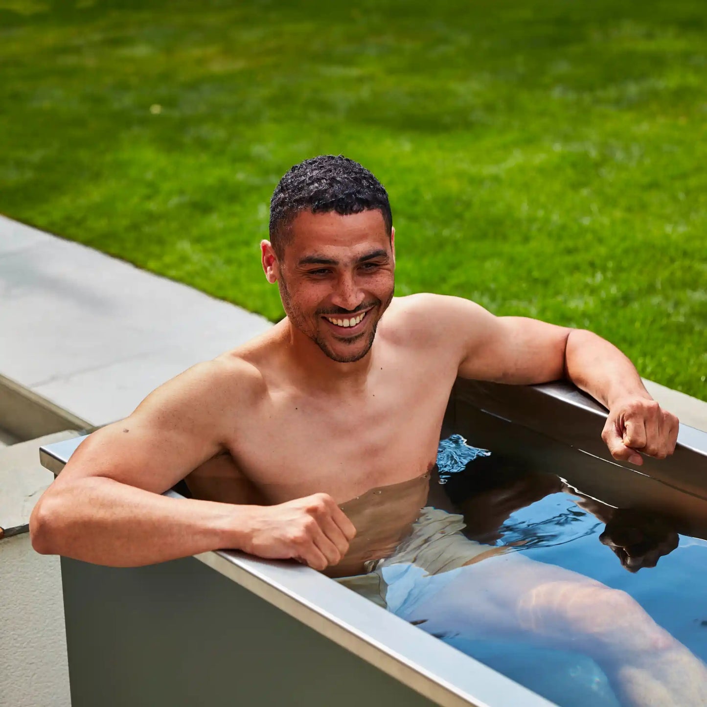 Man relaxing in an ice bath outdoors with green grass in the background