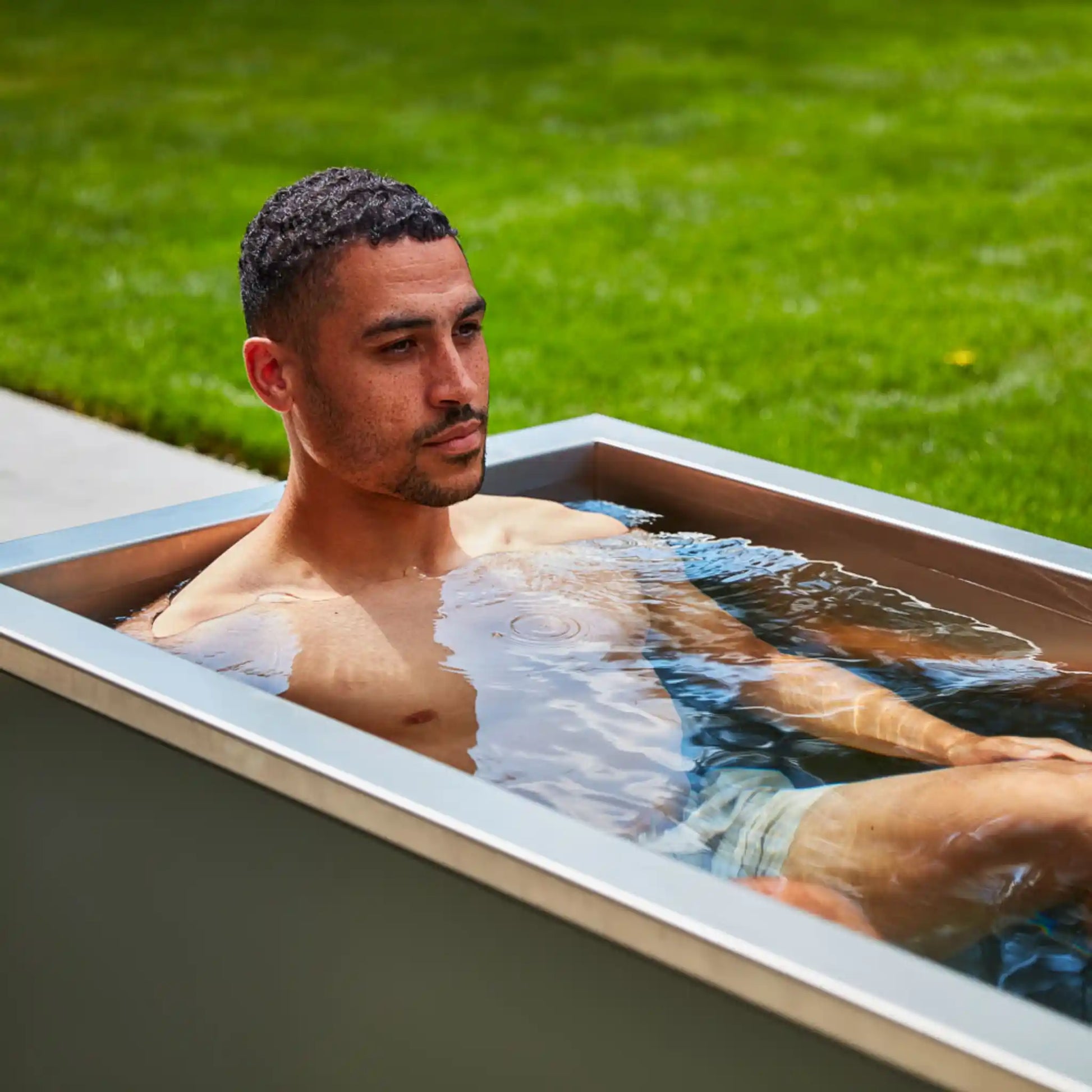 Man relaxing in an ice bath outdoors with green grass in the background