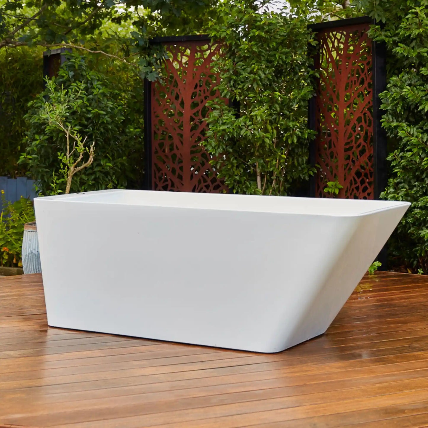 White freestanding ice bath on a wooden deck with greenery in the background