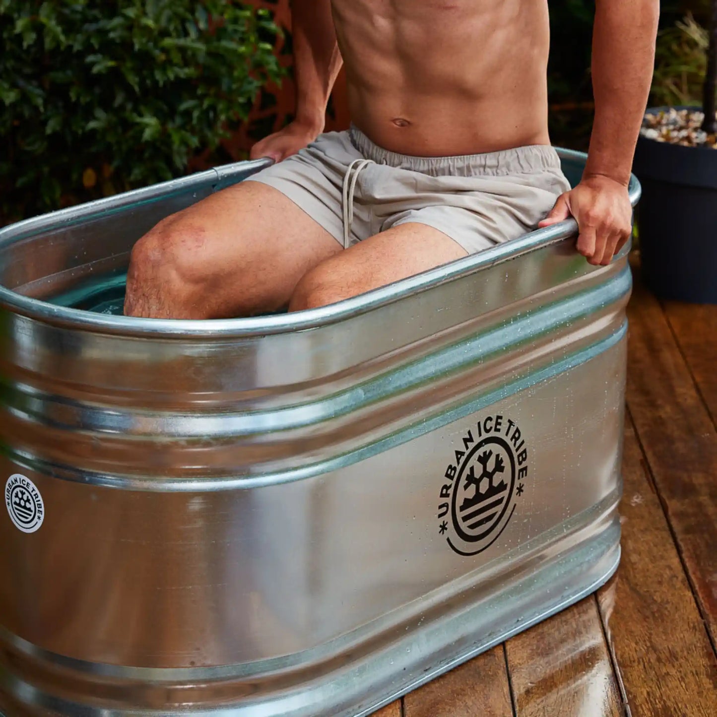 Main getting into a steel ice bath, with Urban Ice Tribe branding, in a garden